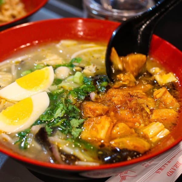 A close-up of Burmese noodle soup with egg, cilantro, and meat in a red bowl.
