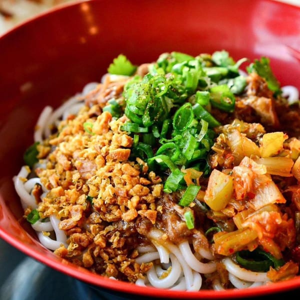 Burmese noodles with crispy fried garlic, green onions, and pickled vegetables in a red bowl.