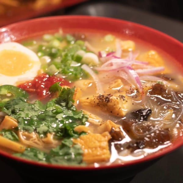 Close-up of a Burmese noodle soup with egg, cilantro, red onions, and tofu in a red bowl.