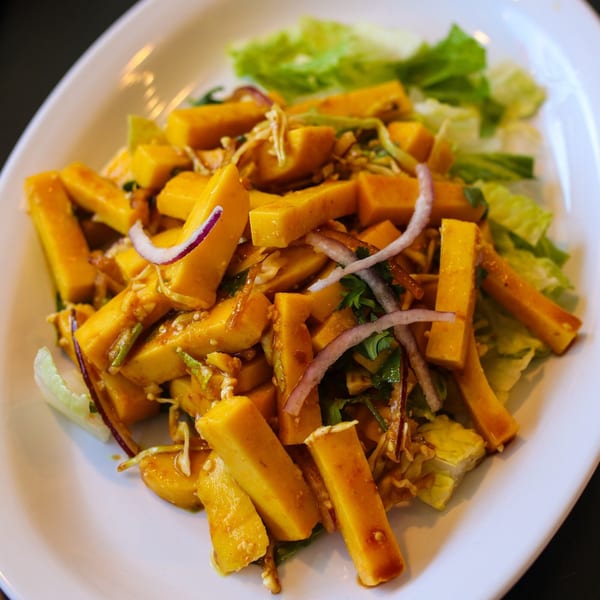 Burmese tofu salad with yellow tofu sticks, red onions, and green lettuce on a white plate.