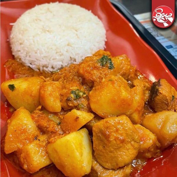 Burmese chicken and potato curry with white rice, served on a red plate.