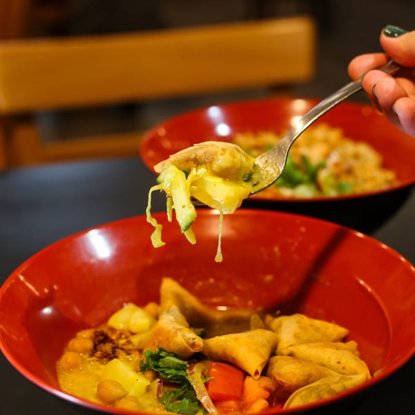A spoonful of Burmese samosa salad with potatoes, chickpeas, and vegetables over a red bowl.
