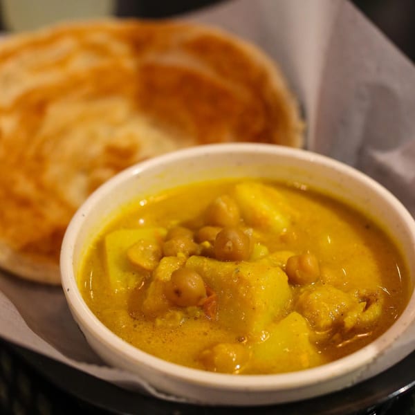 A bowl of Burmese chickpea and potato curry with a side of flaky paratha bread.