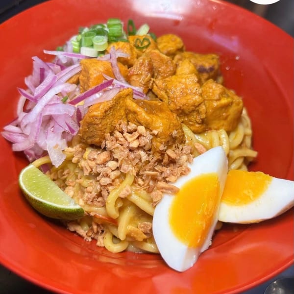 Burmese chicken noodles with red onions, green onions, fried garlic, lime, and a hard-boiled egg.