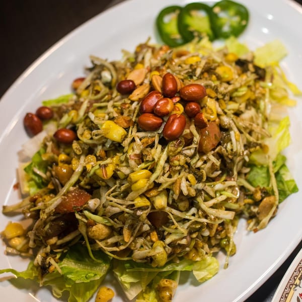 Burmese tea leaf salad with peanuts, corn, and jalapeños on a white plate.